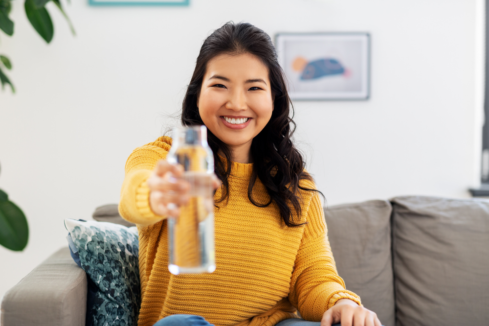 a smiling woman wearing a yellow sweater holding up a glass of fresh water